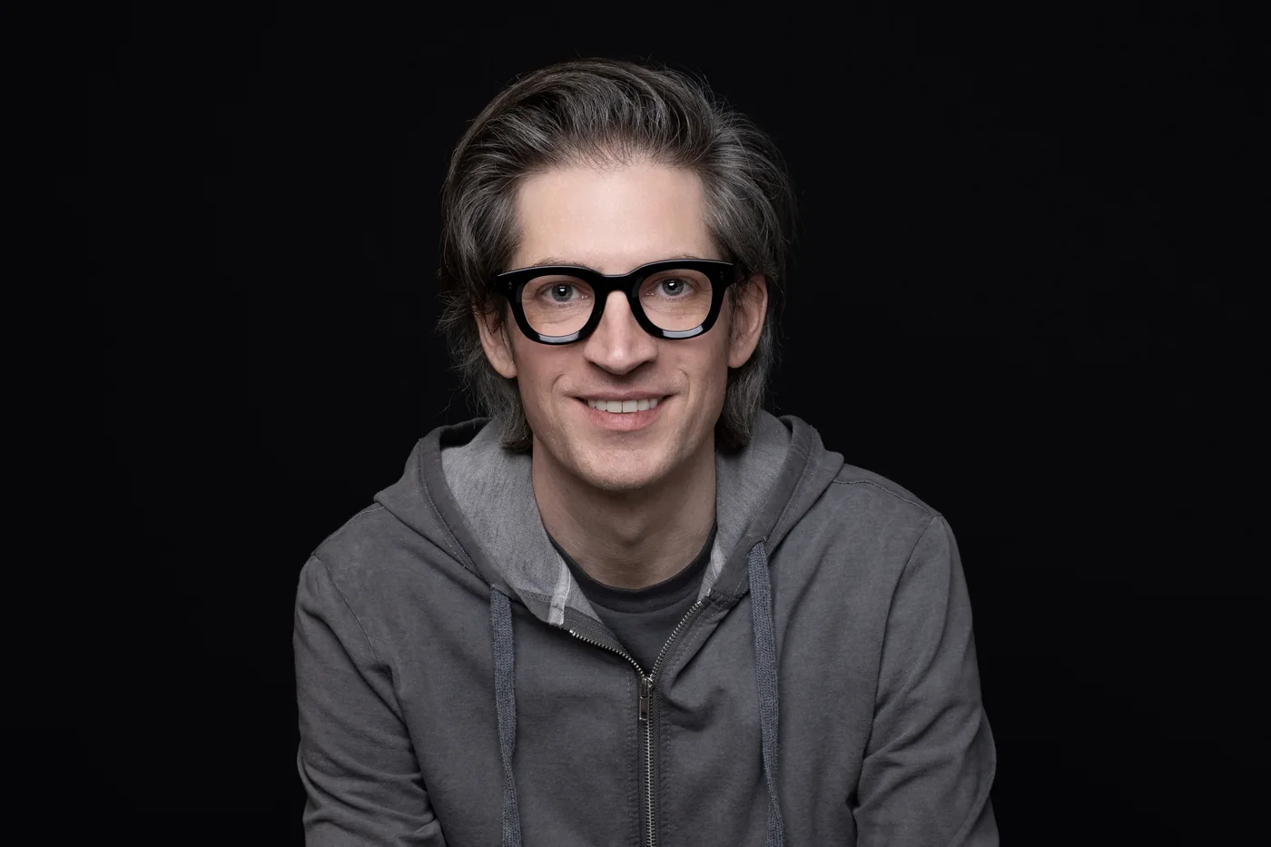 Jake Miller in a grey hoodie and black-framed glasses against a black studio background, the engineer and researcher behind the security work.